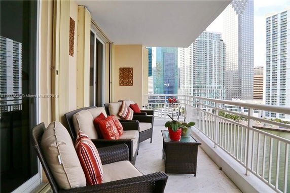 Balcony view from a high-rise apartment overlooking the city with outdoor seating and decorative pillows.