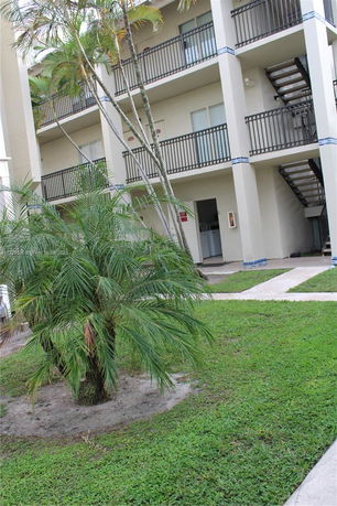 View of a multi-story building with balconies and staircases, surrounded by greenery and palm trees.