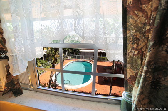 View of a swimming pool through a window with curtains.