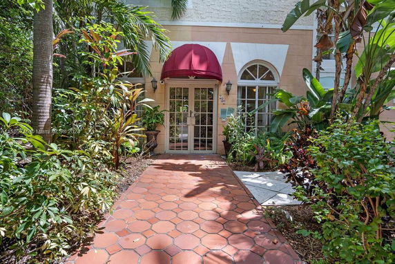 Front view of a building entrance with a red canopy and surrounding plants.