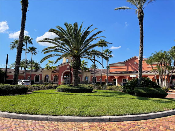 Front view of a large building with arched windows and a tiled roof, surrounded by palm trees.
