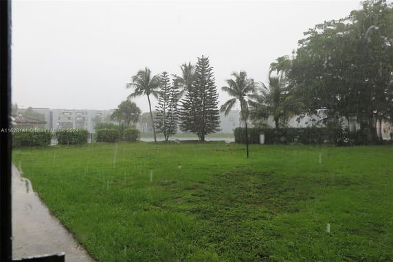 View of a grassy area with trees and distant buildings seen under rain.