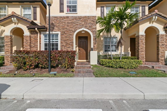 Front view of a townhouse with stone and stucco facade and arched entrance.