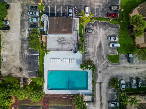 Aerial view of a swimming pool surrounded by a parking area with several parked cars.