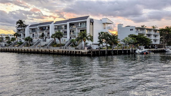 Front view of a waterfront apartment complex with multiple balconies and palm trees.