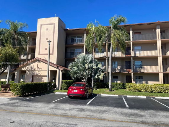 Front view of a multi-story apartment building with balconies and palm trees.