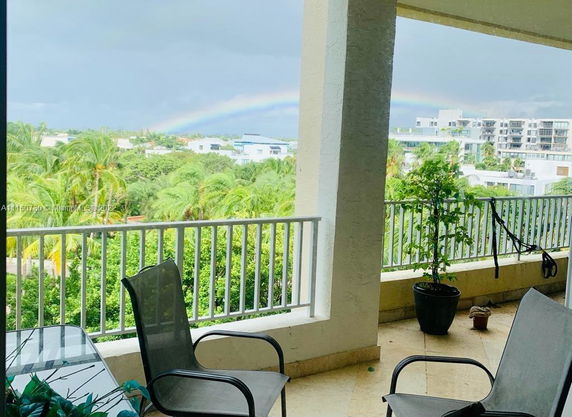 View from a balcony overlooking lush greenery and multiple modern buildings under a cloudy sky with a visible rainbow.