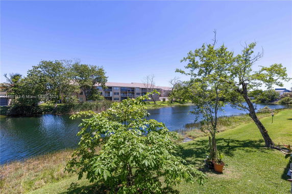 View of a residential building near a lake with green trees and grass.