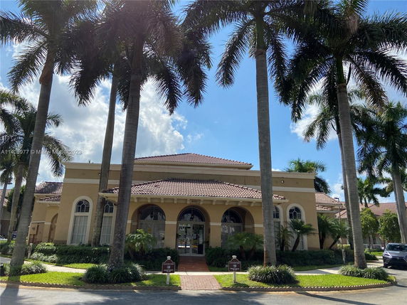 Front view of a large building with arched windows and a tile roof surrounded by tall palm trees.