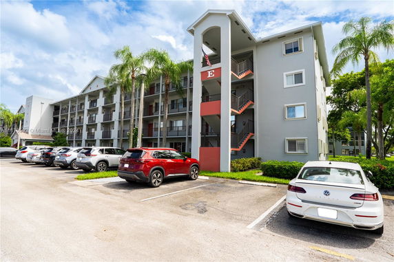 Front view of a multi-story residential building with balconies and parked cars.