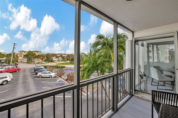 View from a balcony overlooking a parking area with several parked cars and palm trees.