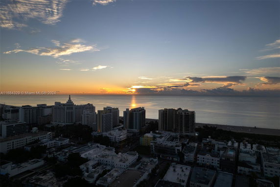 Aerial view of a coastal cityscape with high-rise buildings and a sunrise over the ocean.