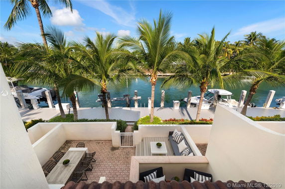 Outdoor area with seating arrangements overlooking a dock and waterway lined with palm trees.