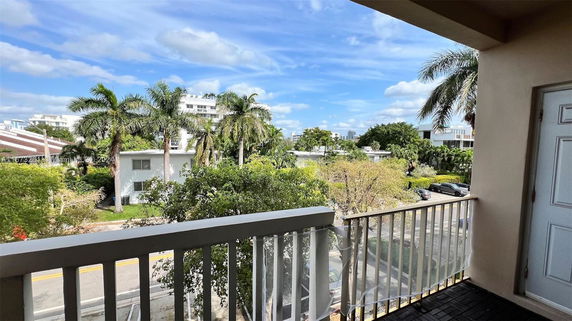 Panoramic view from a building balcony overlooking trees and residential houses.