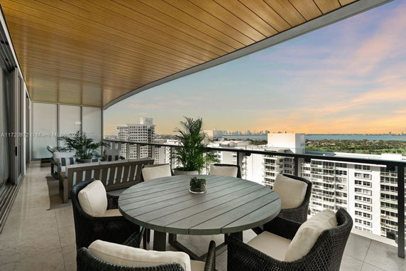 Panoramic view from a high-rise balcony with dining furniture overlooking the city and water.