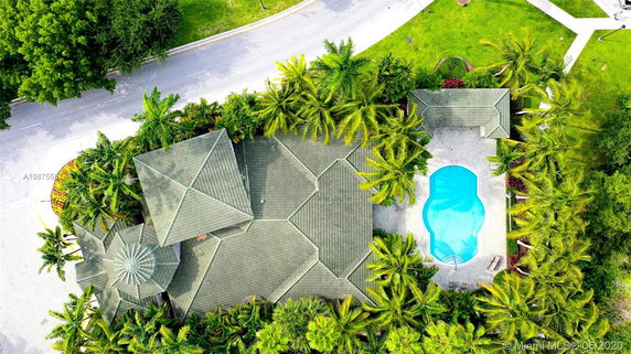 Aerial view of a house with a complex roof structure and a swimming pool surrounded by trees.
