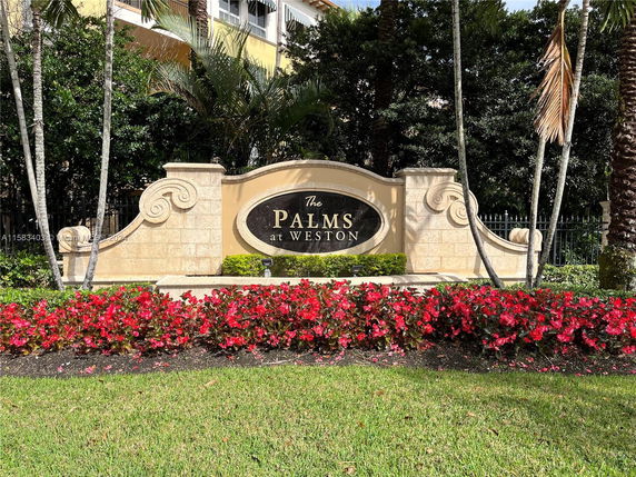 Sign for 'The Palms at Weston' surrounded by flowers and trees.