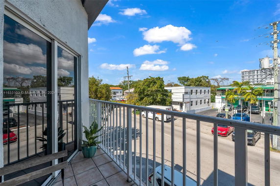 View from a balcony overlooking a street with buildings and parked cars.