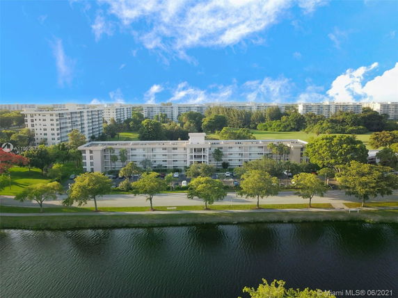 Aerial view of an apartment building surrounded by greenery and a waterfront.