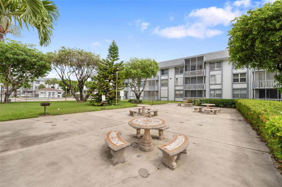 View of a multi-story building with balconies and surrounded by trees and outdoor seating area.
