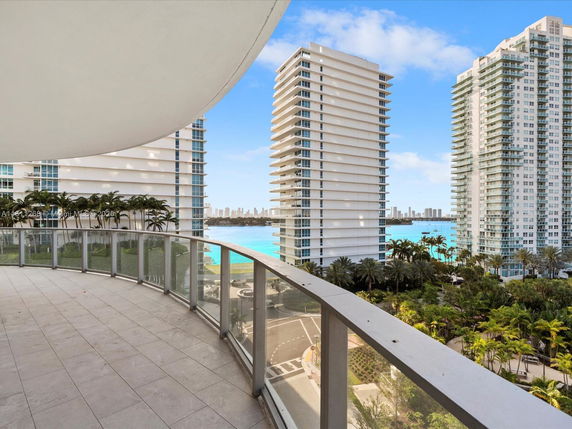 Panoramic view from a building balcony showing nearby high-rise buildings and a water body.