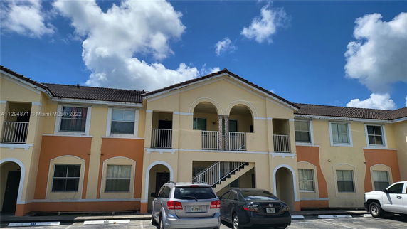 Front view of a two-story apartment building with arched balconies and a tiled roof.