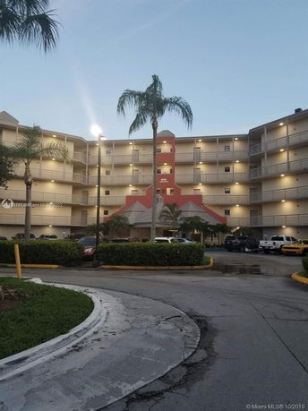 Front view of a multi-story apartment building with balconies and a parking area.