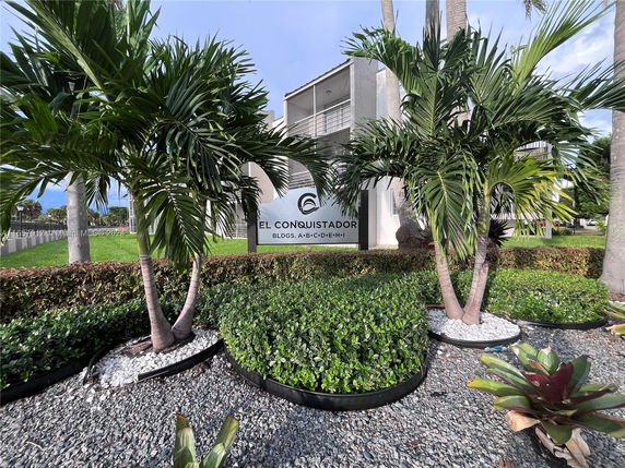 Front view of a building partially obscured by trees with a sign that reads 'El Conquistador.'