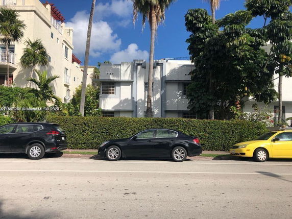 Front view of a multi-story residential building with parked cars on the street.