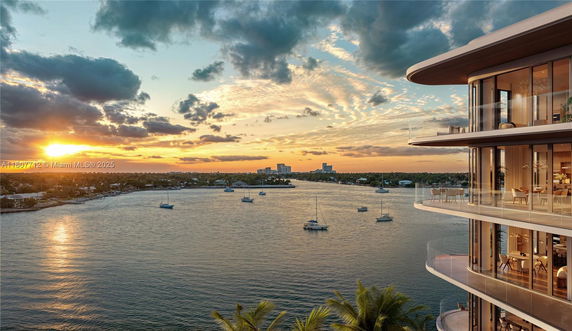 Balconies of a modern apartment building overlooking a body of water with boats and a sunset scene.