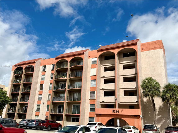 Front view of a multi-story apartment building with balconies and parking area.