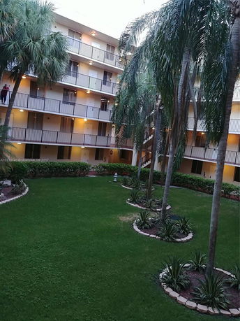 Front view of a multi-story apartment building with balconies and surrounding landscaped area.