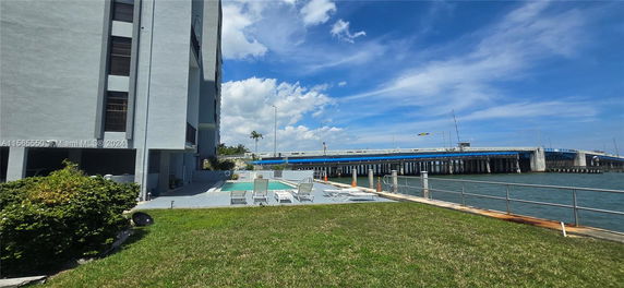 Outdoor swimming pool area next to a building with a view of a bridge over water.