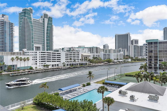 View of modern high-rise buildings near a waterway with a boat and pool area in the foreground.