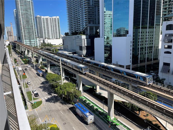 View of a cityscape with tall buildings, elevated train tracks, and a busy street below.