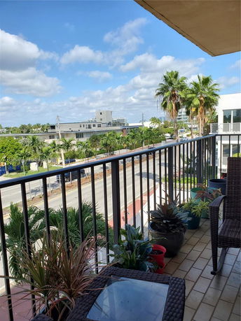 View from a balcony showing a street with buildings and palm trees.