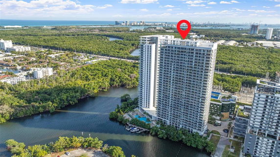 High-rise building surrounded by lush greenery and water bodies.