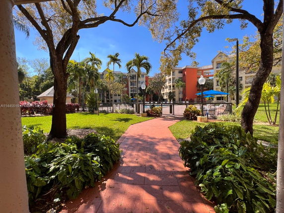 Outdoor view of a landscaped pathway leading to a gated area with a building in the background.