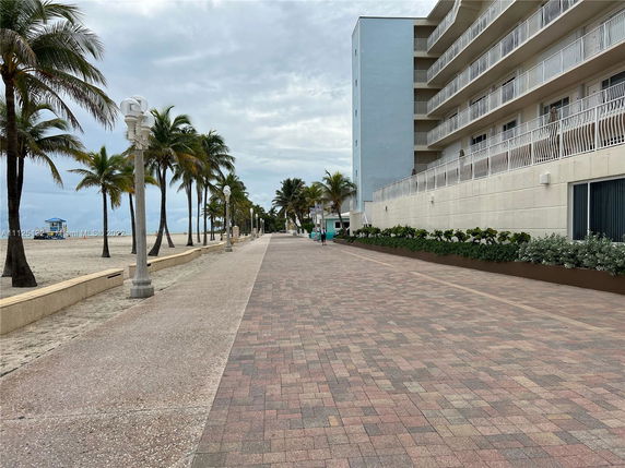 View of a beachfront walkway adjacent to a multi-story building with balconies.