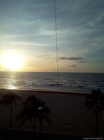 View from a beachfront location showing the ocean and a sandy beach at sunset.