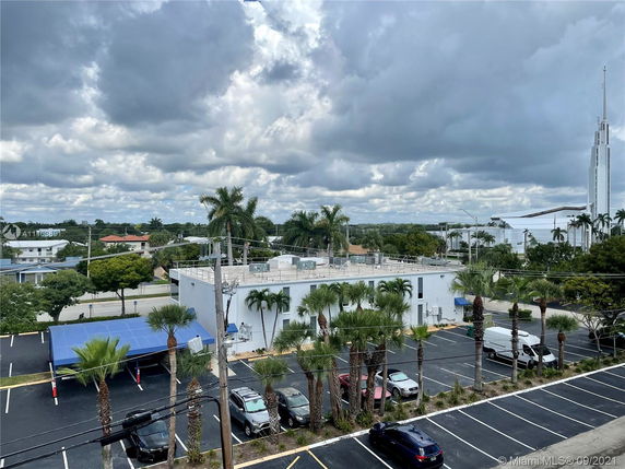 Aerial view of a parking area with a blue-covered parking shade and a white building surrounded by palm trees.