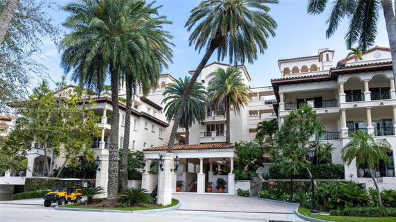 Front view of a multi-story residential building with balconies and decorative arches, surrounded by palm trees.