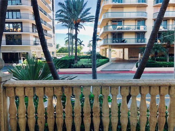 View of a multi-story building with balconies and a driveway, seen from behind a decorative railing.