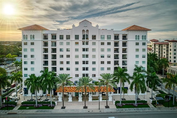 Front view of a multi-story residential building with palm trees in front.