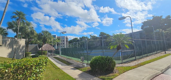 View of a tennis court surrounded by tall buildings and palm trees.