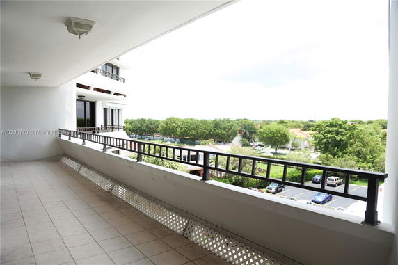 Panoramic view from a balcony overlooking a landscape with trees and parked cars.