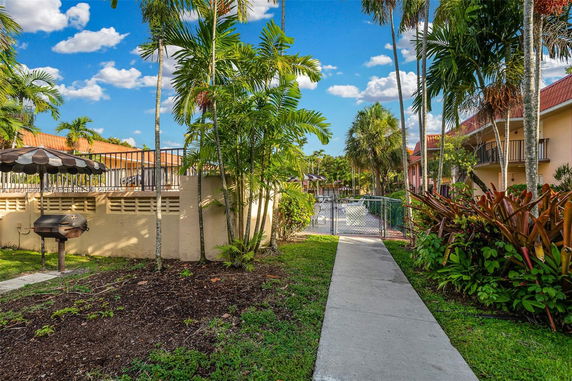 Outdoor area with a walkway leading to a swimming pool surrounded by palm trees and residential buildings.