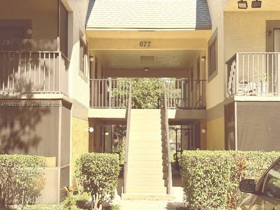 Front view of a building entrance with stairs leading up to a second-floor balcony.