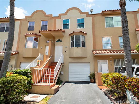 Front view of a multi-story townhouse with a garage and stairs leading to the entrance.