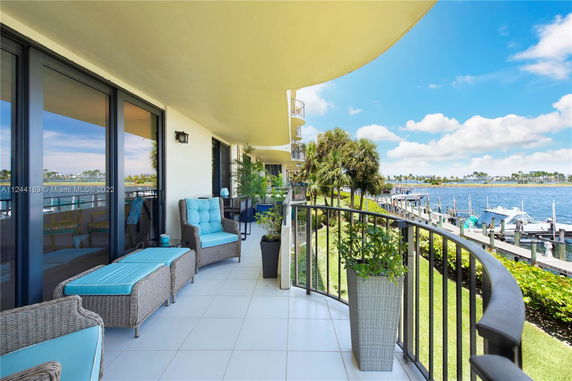 Outdoor balcony area with seating overlooking a waterfront with boats and greenery.